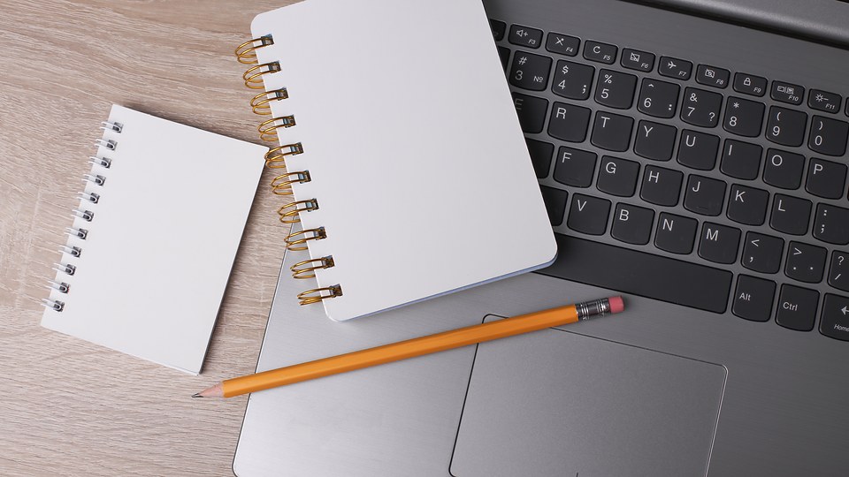 Research notes and a notebook on a laptop — the audit and scoping work before any project begins